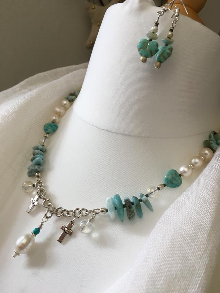 A turquoise, pearl and sterling silver necklace with matching drop earrings, arranged on a cream dress form.