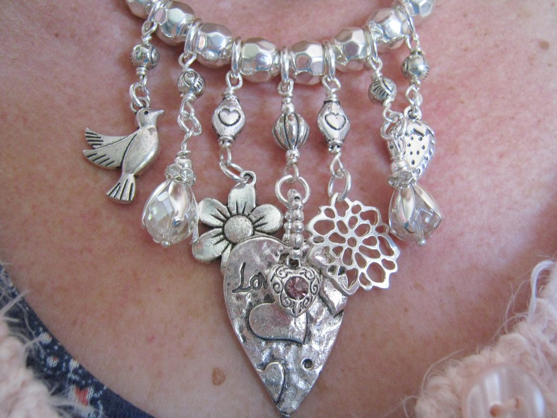 A sterling silver charm necklace worn at the collarbone, hung with a bird, a flower and a heart pendant.