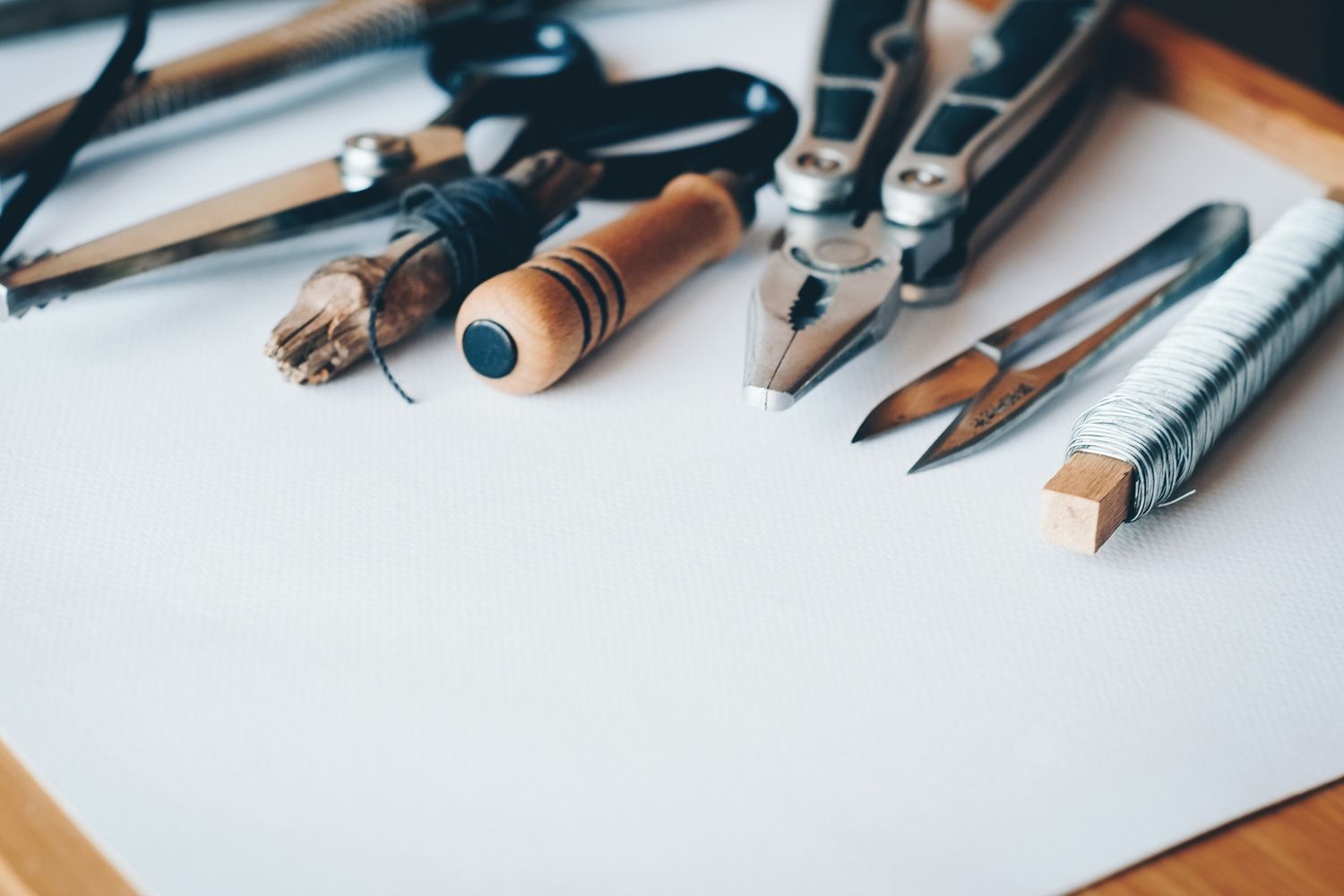 Jewellery-making tools laid out on a workbench — pliers, snips, wire and a wooden burnisher.